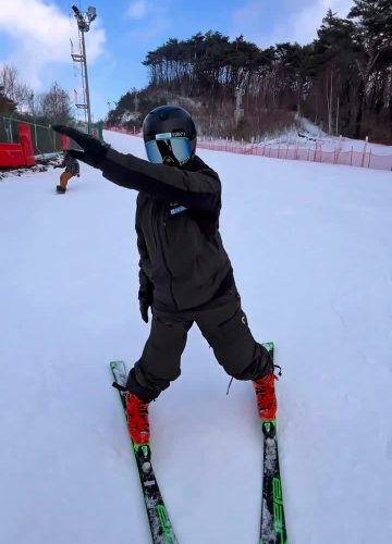 A skier in black opens the skis and extends one arm during a ski balance challenge on snow in Korea