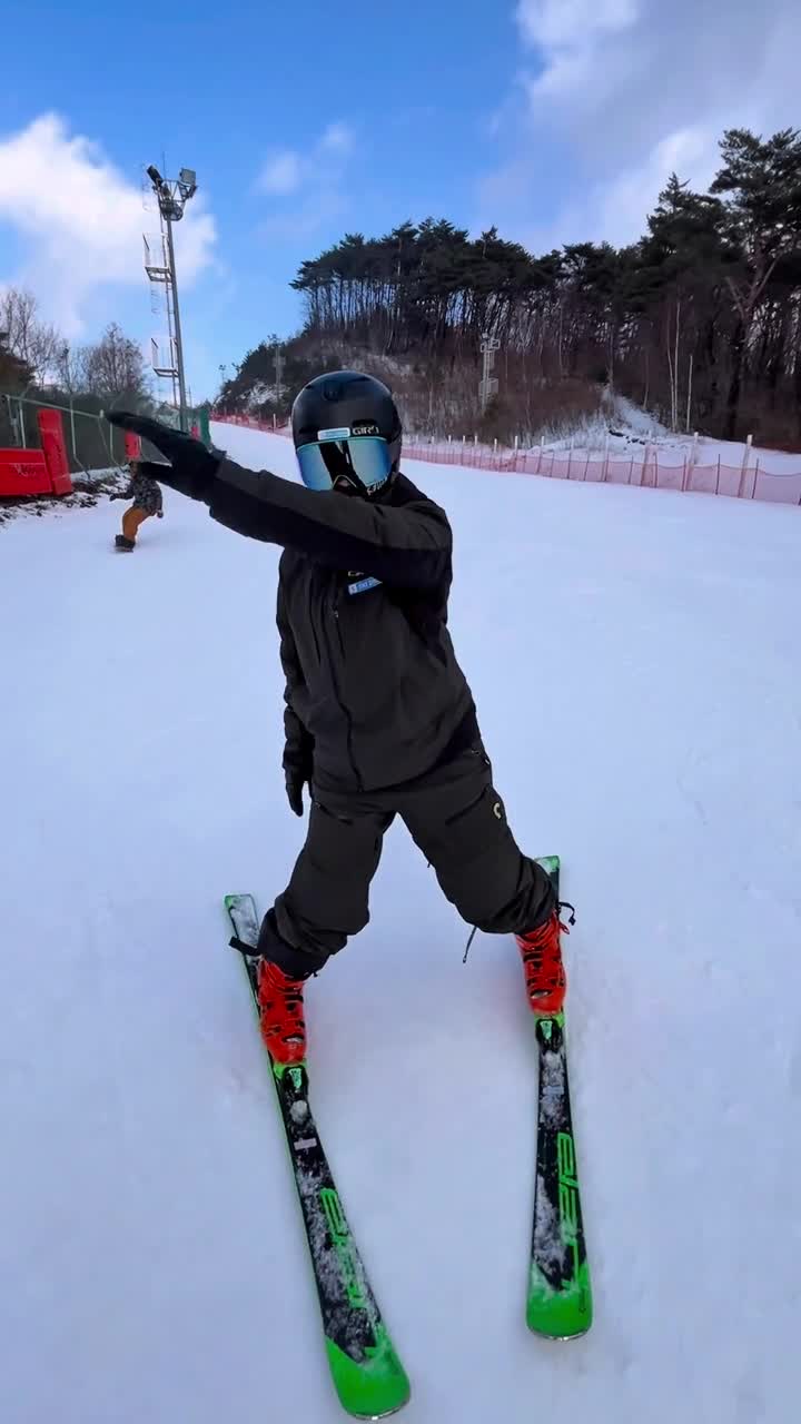 A skier in black opens the skis and extends one arm during a ski balance challenge on snow in Korea